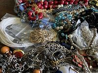 Lot of mixed jewelry including varied bead necklaces, chains, and bracelets mostly piled on a surface with some plastic bag storage visible.