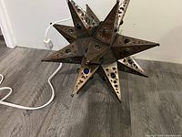 Side view of metal star-shaped lamp with blue and green glass beads, power cord and switch visible.