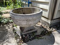 Side angle view of the round vintage outdoor planter showing its shape, surface wear, and base.