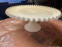 View of vintage white milk glass cake stand showing ruffled edge and pedestal base
