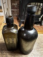 Front and side view of rectangular Aromatic Schnapps bottle and round deep green glass bottle shown on wooden surface