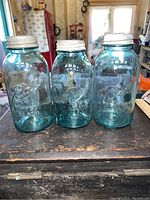 Front view of three deep blue 1/2 gallon Ball Perfect Mason jars with zinc lids on a wooden surface.