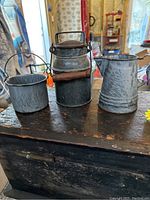 Three gray graniteware items including a cream can with wooden handle, a berry pail with wire handle, and a cowboy coffee pot without lid.