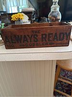 Wooden box front long side showing 'THE ALWAYS READY 100 COBBLER TRADEMARK' text.