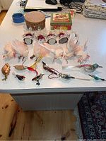 Overview of lot with multiple antique glass bird ornaments and homemade crocheted-wing angels on white countertop with two decorative boxes in background