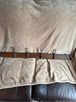 Full view of the oak and cast iron coat rack with four triple hooks placed horizontally on a beige fabric surface.