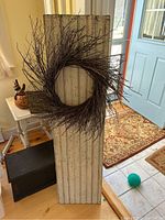 Photo of the full shutter standing upright with the twig wreath hanging centrally on it, showing the shutter's full height and narrow width along with the distressed paint.