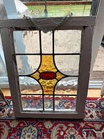 Front view of antique stained glass window showing entire piece with wooden frame and chain hanging.