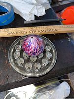 Top down view of a large antique swirl marble on a glass holder with a wooden ruler for size reference approximately 2 inches.