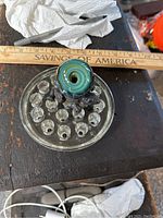 View of the top and side of the glass marble placed on the clear stand with multiple round indentations, showing intricate swirling glass patterns, colors, and details of the supporting figurine beneath the marble.