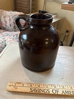 Front side view of the brown Albany slip glazed oyster jar showing the body and handle with a ruler for scale.