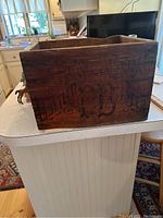 Wooden beer crate placed on a kitchen countertop with visible ornate stencil text on the side showing letters and partial branding.