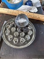 Full view of the glass paperweight on a dark surface with measuring ruler and items in background.