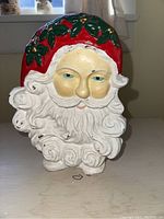 Front view of cast iron Santa Claus door stop showing detailed face, beard, and painted red hat with green holly and gold berries.
