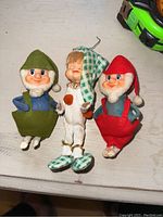 Photo showing the full lot with the boy doll in green and white checkered nightcap and slippers, flanked by two rubber faced dwarves in red and green outfits.