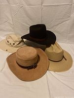 Four assorted hats arranged together on white cloth background, showing different styles and materials.