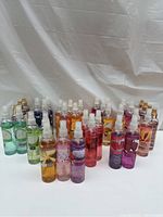 Lot of 31 Avon body spray mist bottles arranged on white cloth backdrop showing assorted colors and labels.