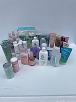 Front view of assorted beauty and personal care products including sprays, lotions, powders, and deodorants arranged on a white surface