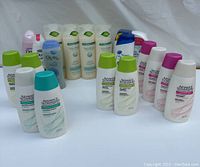 Lot of unopened body wash and shampoo bottles from multiple brands arranged in rows on a white fabric background.