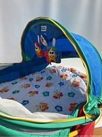 Blue and green Fisher Price baby tent with padded white mat featuring butterfly and flower designs, attached blue canopy with hanging plush toys visible from side angle.