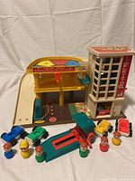 Full view of the Fisher Price Parking Ramp playset, accessories including elevator, vehicle lift, five toy cars, and six Little People figures in various colors and outfits.