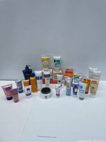 Wide shot showing 18 assorted cream tubes, bottles, and jars mainly for hand, foot, and body care including Dove, O'Keeffe's, and others.