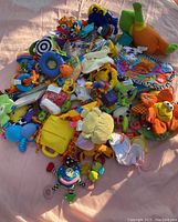 Top view of a large pile of various colorful baby educational toys such as stuffed animals, sensory rings, and soft learning books placed on a fabric surface.