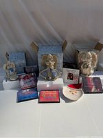 Wide shot of the Christmas lot showing three angel figurines, some holiday CDs, and a Santa plate arranged on a covered surface with boxes behind.