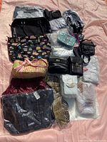 Photo showing multiple assorted purses including black leather styles, a woven basket-style purse, and various items in original packaging spread on a surface.