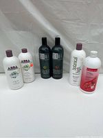 Photo shows six assorted shampoo and conditioner bottles from various brands including ABBA, SOMA, and Naturals. Bottles differ in color and design, some labeled with botanical themes.
