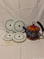 Photo showing the carnival carousel themed stove top kettle and four white stove burner covers with black floral borders.