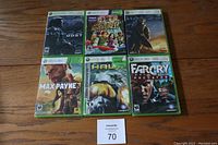 Six Xbox 360 game cases arranged on floor showing front covers, titles visible including Halo 3: ODST, Kinect Adventures, Alan Wake, Max Payne 3, Halo 3, Far Cry Primal.
