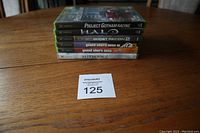 Stacked original Xbox games on wooden table: Project Gotham Racing, Halo, Ghost Recon 2, Grand Theft Auto 3 and Vice City, Hitman 2