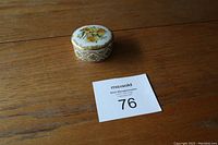 Closed ceramic trinket box showing floral design on lid and golden diamond pattern on side.