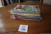 Photo showing a stack of mixed comics on a wooden table, with item number card.