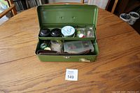 Open green metal tackle box showing fishing hooks, lines, sinkers and small containers inside.