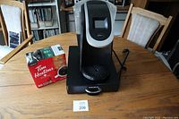 Front view of Keurig coffee maker on metal stand with drawer, next to box of Tim Hortons K Cups on wooden table.