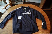 Full view of navy blue zip-up sweater with Canada text and two pockets laid out on a wooden table.