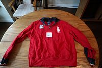 Red Polo sweater laid flat on wooden table, showing front full view.
