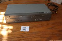 Magnavox DVD VHS Player showing top and front panel on wooden table with auction lot card 219