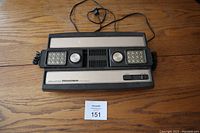 View of Mattel Intellivision console from front with attached power cable visible and two controllers resting on console top panel, showing numeric keypads and directional pads.