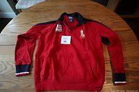 Full view of red long-sleeve Polo sweater laid flat showing front side, embroidered logos and cuffs detail.