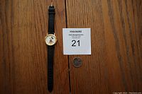 Full view of the Lorus Mickey Mouse watch laid flat on a wooden surface with a quarter for size reference and a note card labeled '21'.