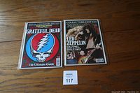 Front view of two magazines: one Grateful Dead special edition and one Led Zeppelin special edition, both in protective plastic sleeves on wooden surface.