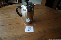 Full view of the stainless steel French press coffee maker with black handle and plunger knob on wooden table next to a quarter coin for scale.