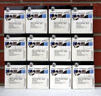 Photo of all twelve Sharp UXC70B black toner cartridges in original boxes, arranged in three rows of four against a brick background.