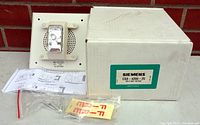 Photo showing the Siemens strobe speaker alarm device next to its original white box, spec sheet, mounting screws, and labels.