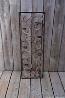 Front view of the vintage iron candle holder showing decorative oval loops and multiple candle platforms within a rectangular frame against a wooden fence background.