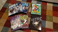 Photo shows all seven DVD sets arranged on a colorful patterned carpet, featuring TV series and anime including Hawaii Five-O (seasons 1-3), The Super Mario Bros Super Show Volume 2, South Park (seasons 4 and 7), and the complete Astro Boy series.