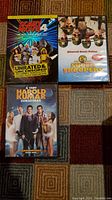 Photo showing three comedy DVDs: Scary Movie 4, Super Troopers, and A Very Harold & Kumar Christmas on a multicolored carpet.